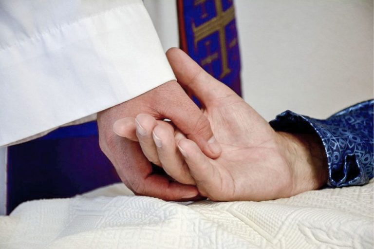 Priester houdt de hand van een zieke vast