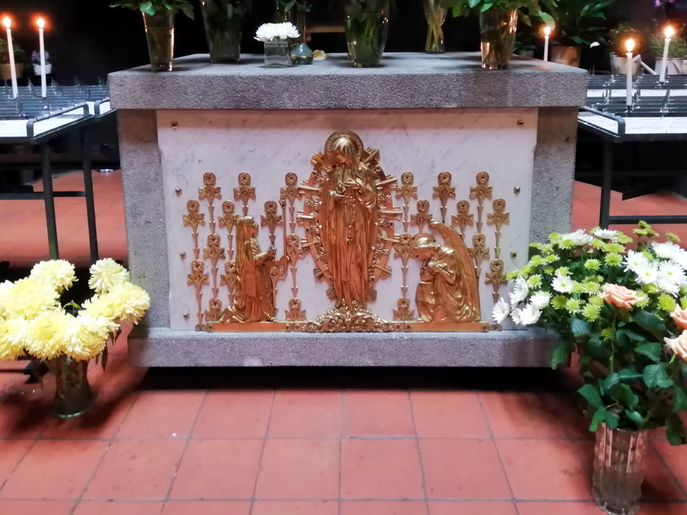 Het altaar van de Lourdesgrot met een verguld Mariarelief en bloemen