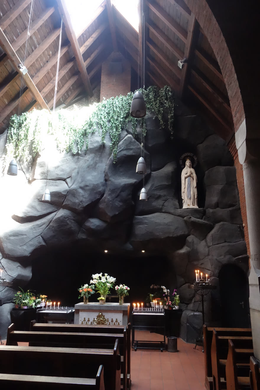 De nagebouwde Lourdesgrot in de kapel met het beeld van Onze Lieve Vrouw van Lourdes, kaarsen en bloemen